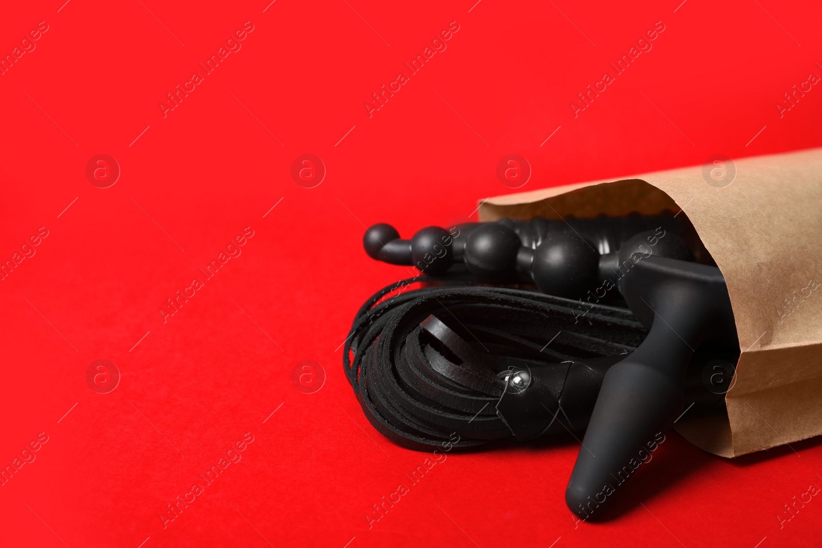 Photo of Paper shopping bag with different sex toys on red background. Space for text