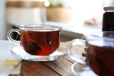 Photo of Tea bag in glass cup on wooden table indoors, closeup