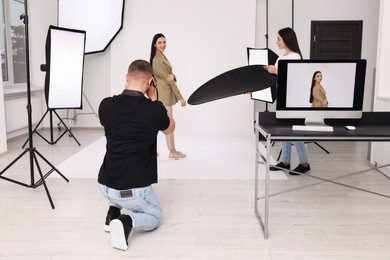 Photo of Professional photographer and assistant working with beautiful model in modern photo studio