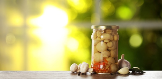 Image of Jar of tasty pickled mushrooms on wooden table in kitchen, space for text. Banner design