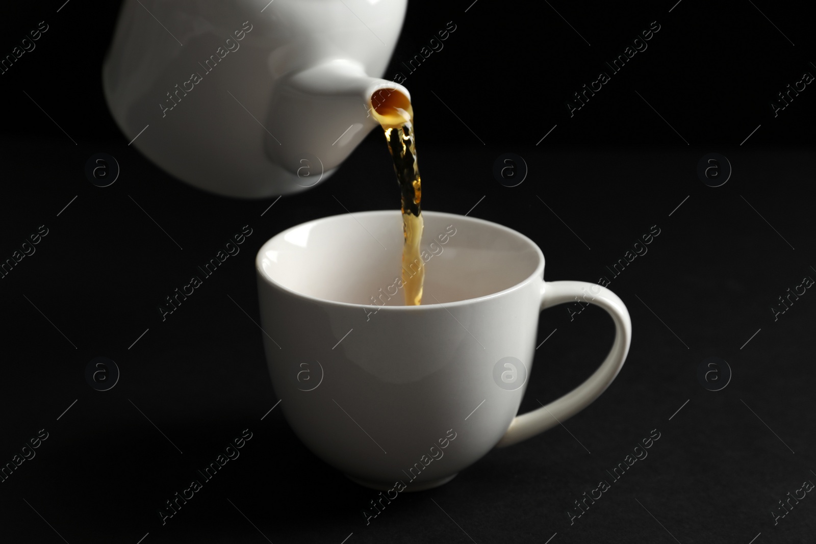 Photo of Pouring hot tea into white porcelain cup on dark background