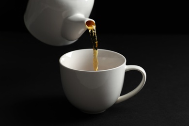 Photo of Pouring hot tea into white porcelain cup on dark background