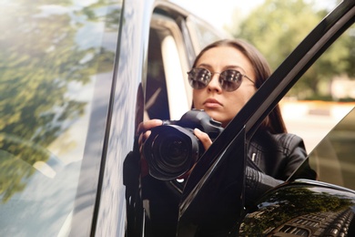 Private detective with camera spying near car outdoors