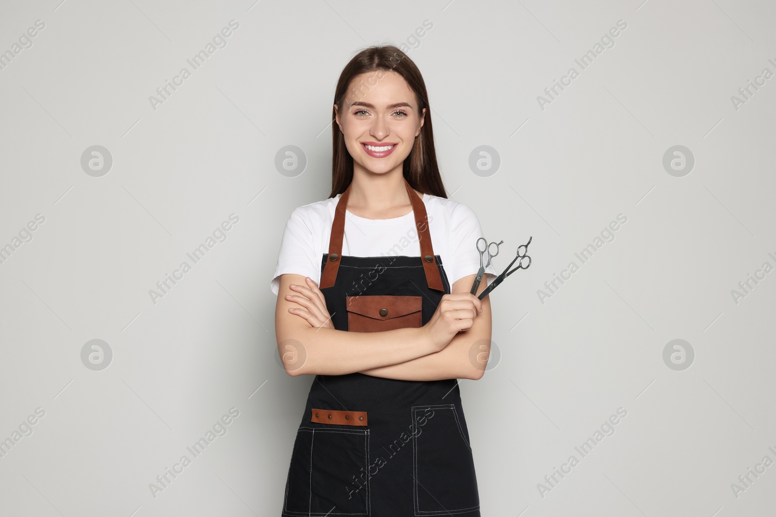 Photo of Portrait of happy hairdresser with professional scissors on light background