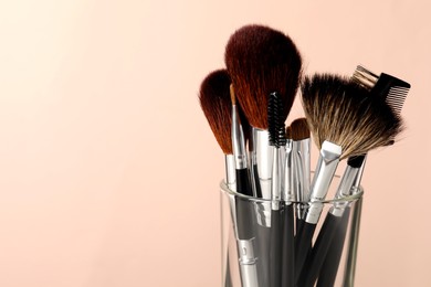 Photo of Set of professional makeup brushes against beige background, closeup. Space for text