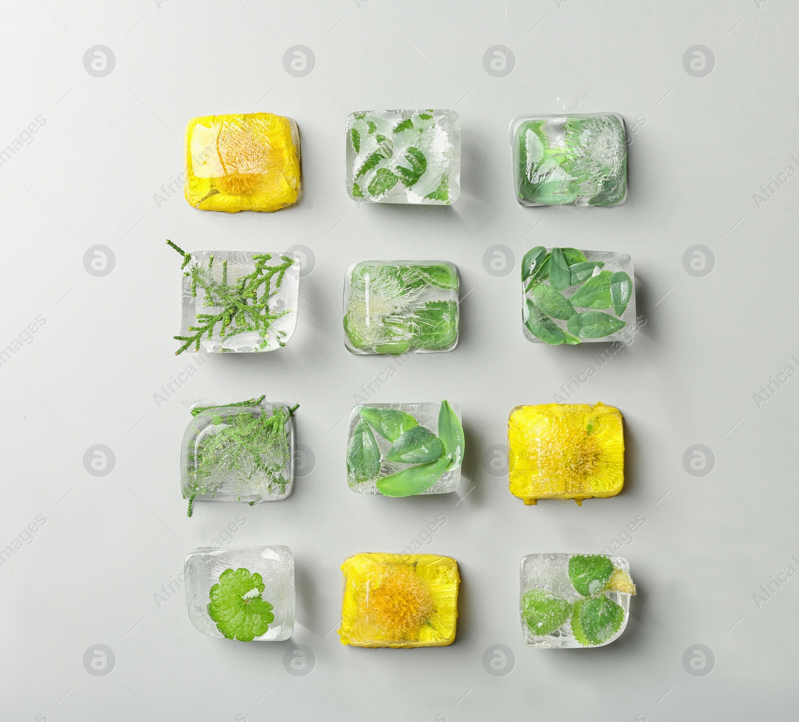 Photo of Ice cubes with flowers and leaves on grey background, flat lay