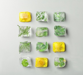 Photo of Ice cubes with flowers and leaves on grey background, flat lay