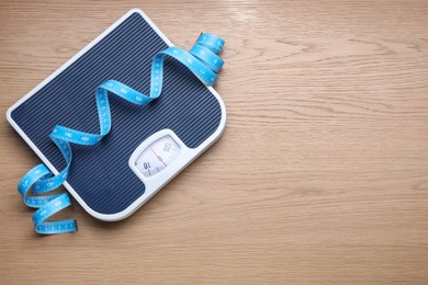 Photo of Scales and measuring tape on wooden background, top view. Space for text