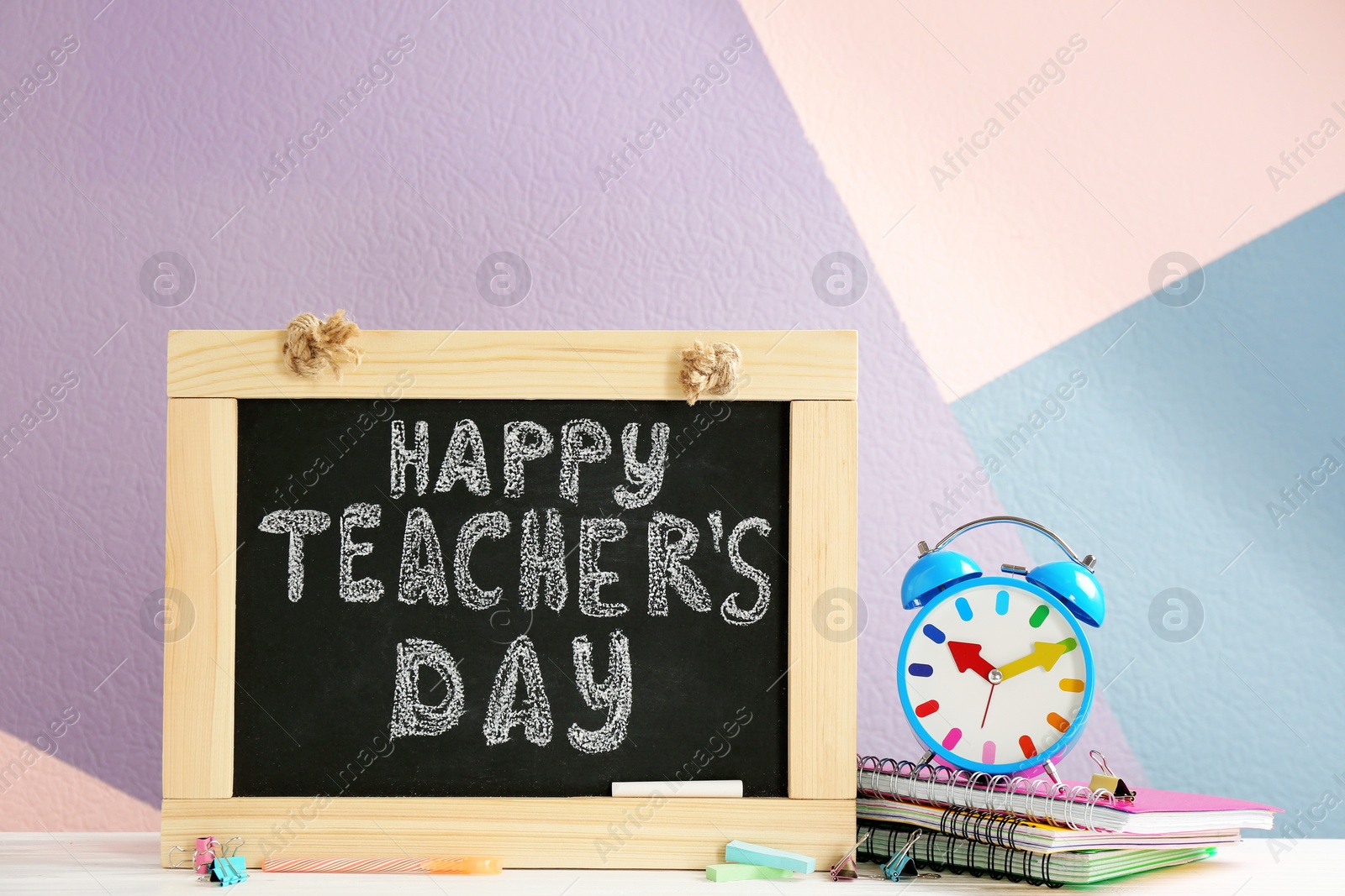 Photo of Little blackboard with inscription HAPPY TEACHER'S DAY, alarm clock and notebooks on table