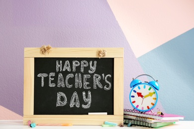 Little blackboard with inscription HAPPY TEACHER'S DAY, alarm clock and notebooks on table