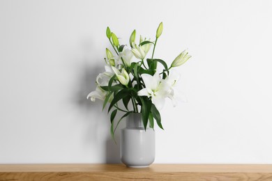Photo of Beautiful bouquet of lily flowers in vase on wooden table near white wall