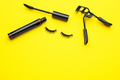 Photo of False eyelashes, curler and mascara on yellow background, flat lay. Space for text