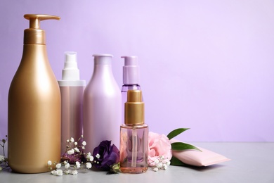 Photo of Set of hair cosmetic products and flowers on grey stone table against violet background