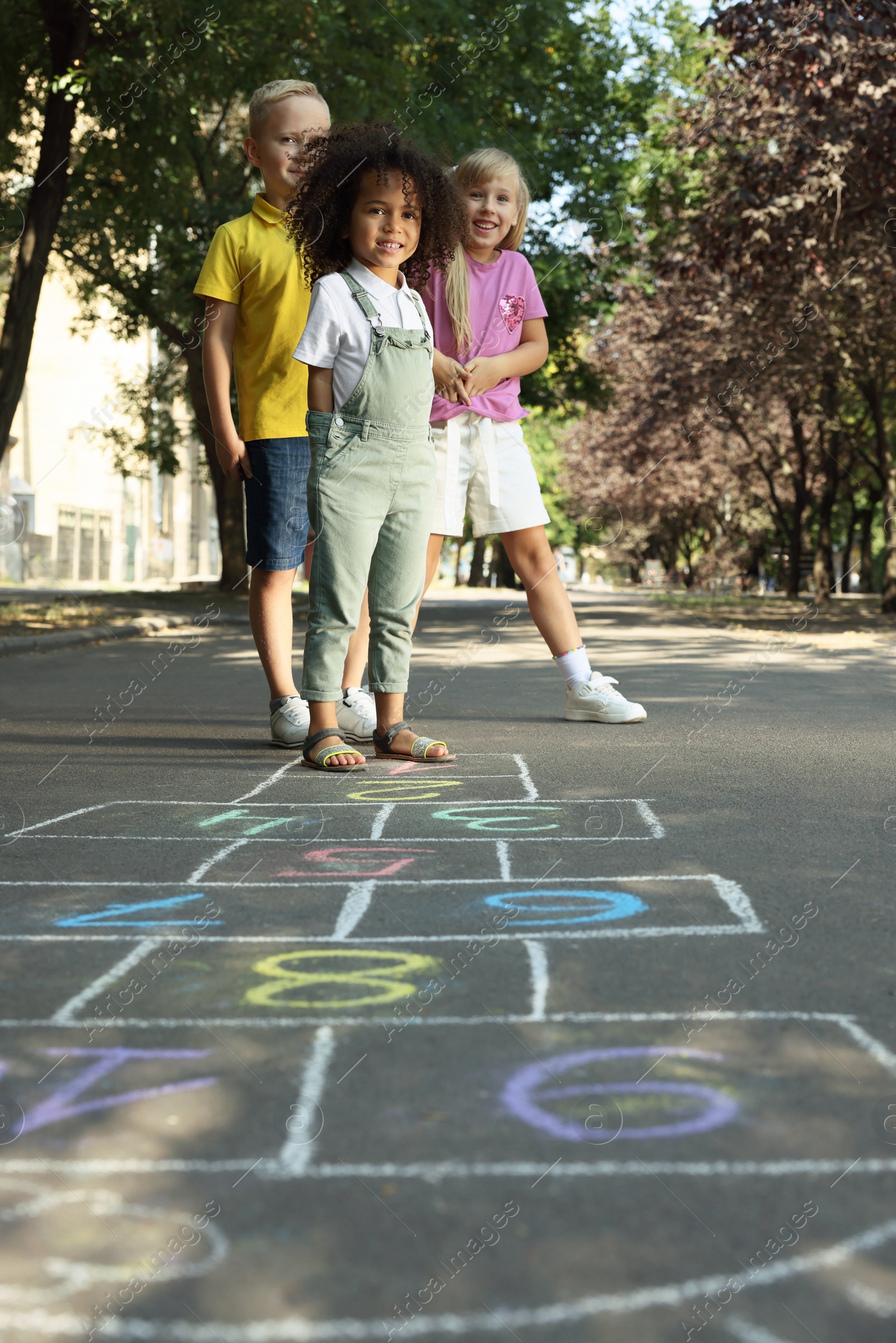 Photo of Little children playing hopscotch drawn with chalk on asphalt outdoors