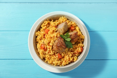 Photo of Bowl with delicious rice pilaf on wooden background, top view