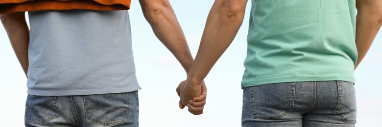 Image of Gay couple holding hands together near river on sunny day, back view. Banner design