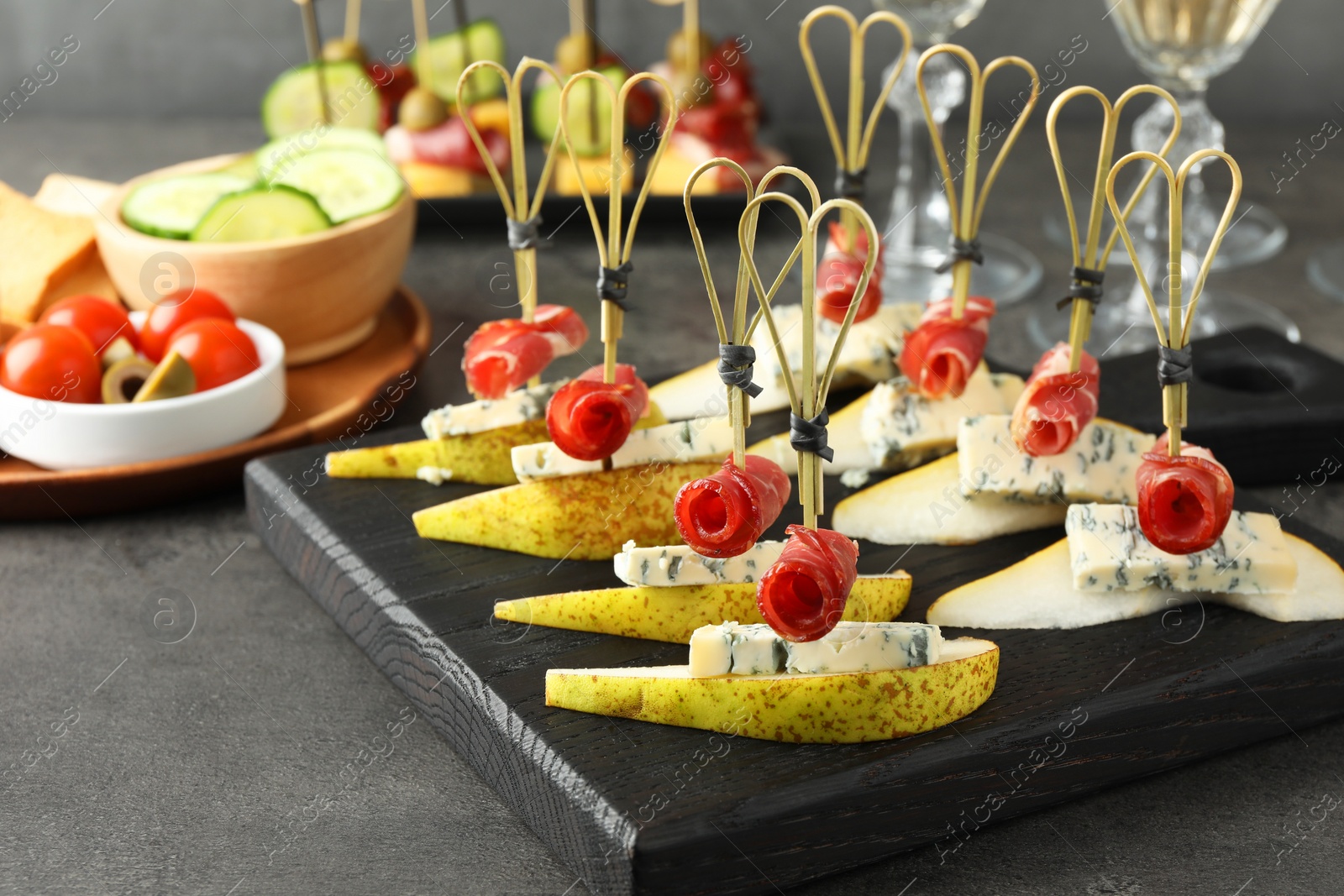 Photo of Tasty canapes with pears, blue cheese and prosciutto on grey table, closeup