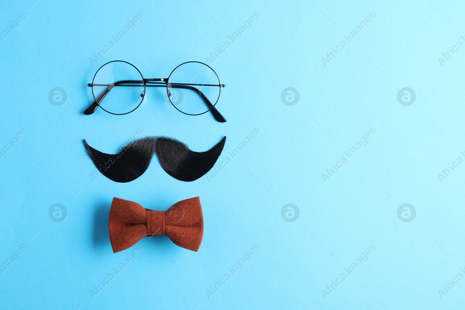 Photo of Artificial moustache, bowtie and glasses on light blue background, flat lay. Space for text