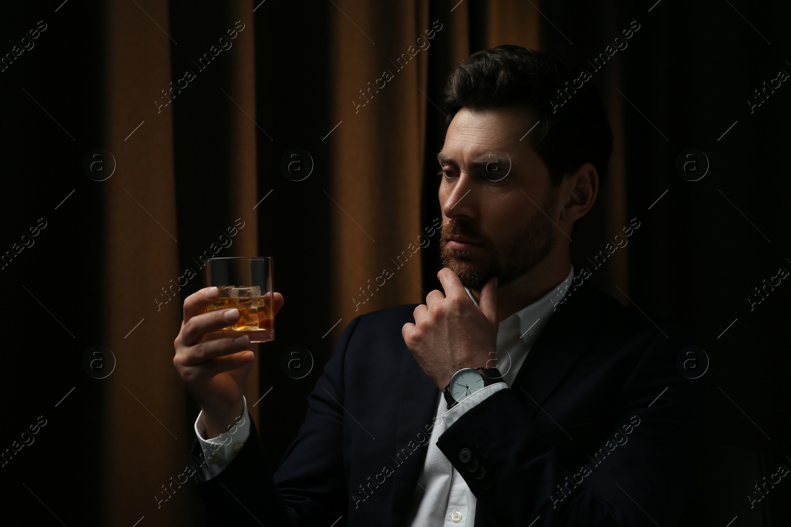 Photo of Man in suit holding glass of whiskey with ice cubes on brown background