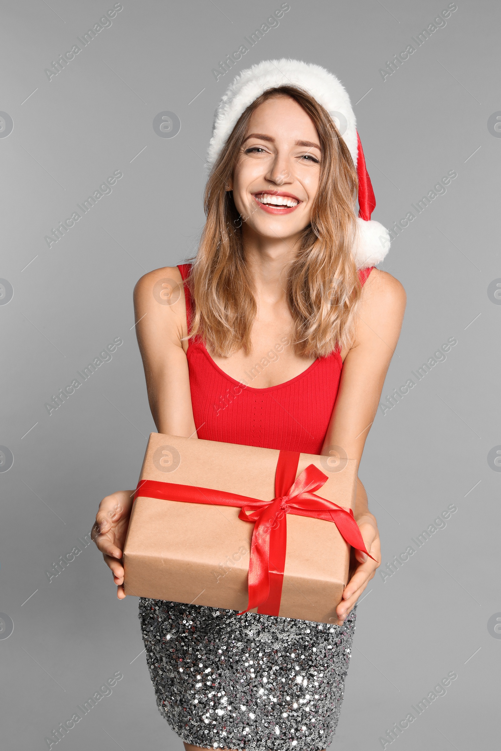 Photo of Happy young woman in Santa hat with gift box on light grey background. Christmas celebration