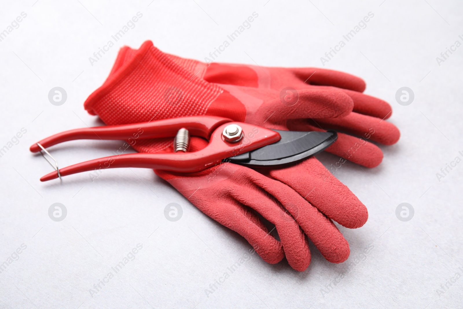 Photo of Pair of red gardening gloves and secateurs on light grey table