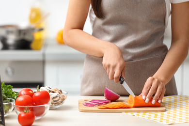 Young woman cutting vegetables for soup at table in kitchen, closeup