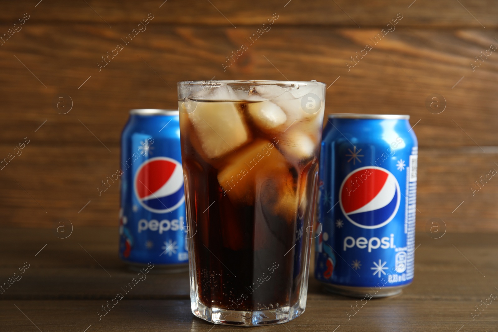 Photo of MYKOLAIV, UKRAINE - FEBRUARY 10, 2021: Glass and cans of Pepsi on wooden table