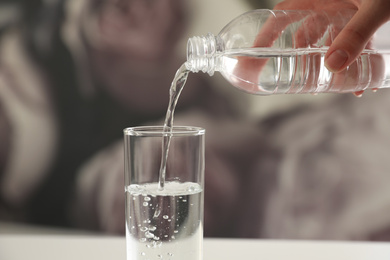 Photo of Woman pouring water from bottle into glass against blurred background, closeup