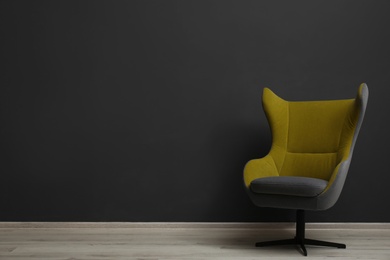 Comfortable office chair near black wall indoors. Space for text