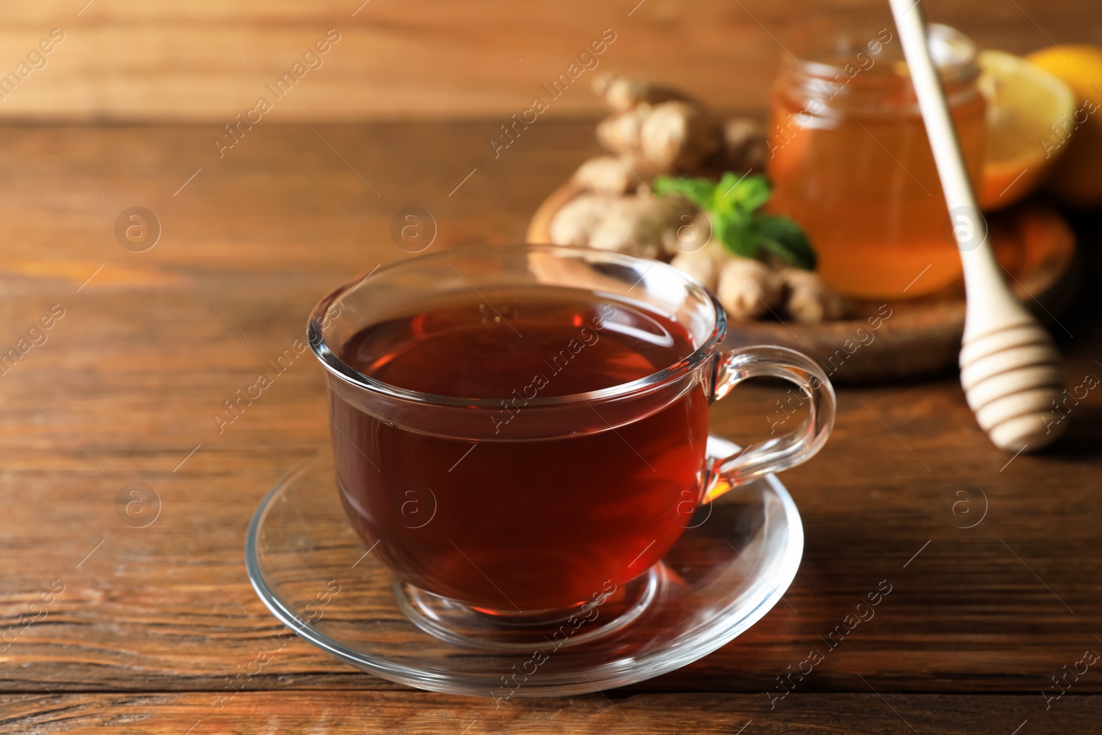 Photo of Cup of delicious ginger tea and ingredients on wooden table