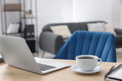 Photo of Home workspace. Laptop, cup of coffee and stationery on wooden desk indoors