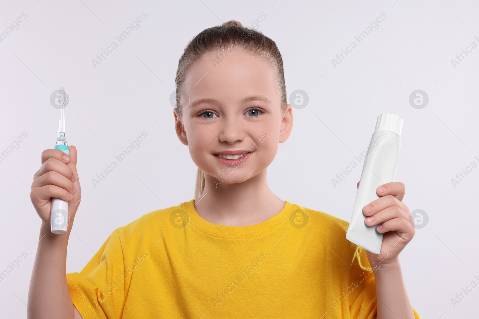 Photo of Happy girl holding electric toothbrush and tube of toothpaste on white background