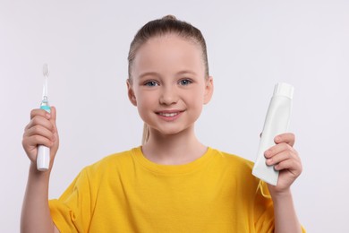 Happy girl holding electric toothbrush and tube of toothpaste on white background