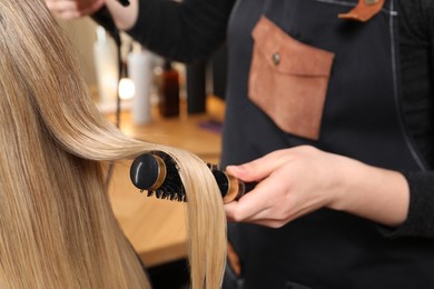 Hairdresser blow drying client's hair in salon, closeup