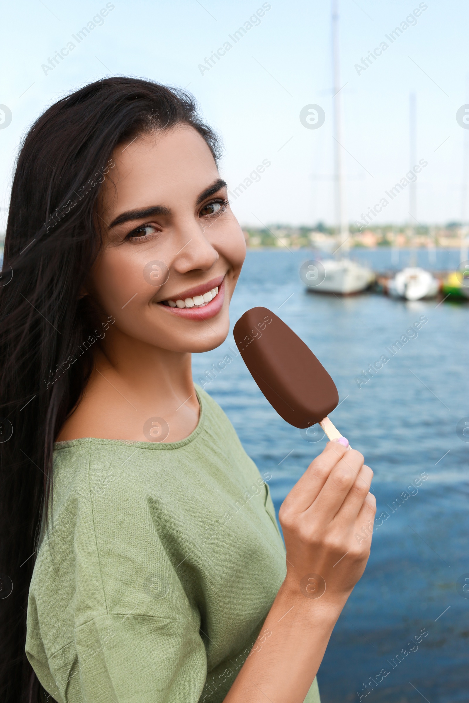 Photo of Beautiful young woman holding ice cream glazed in chocolate near river