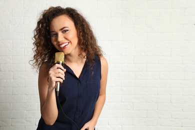 Portrait of curly African-American woman in blouse posing with microphone near brick wall. Space for text