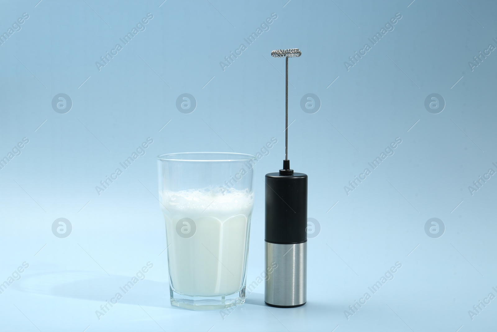 Photo of Mini mixer (milk frother) and whipped milk in glass on light blue background