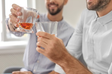 Photo of Friends toasting with glasses of whiskey indoors, closeup