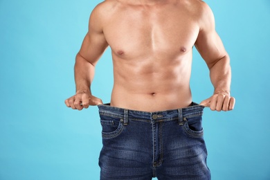 Young man with slim body in old big size jeans on light blue background, closeup view. Space for text