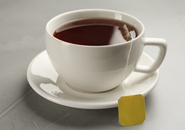 Photo of Tea bag in ceramic cup of hot water on grey table