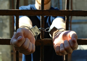 Photo of Man handcuffed in jail outdoors, closeup. Criminal law