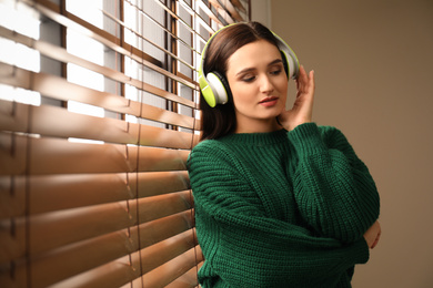 Photo of Young woman listening to audiobook near window indoors