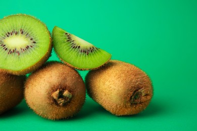 Photo of Heap of whole and cut fresh kiwis on green background, closeup