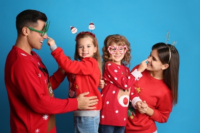 Photo of Family in Christmas sweaters and festive accessories having fun on blue background
