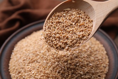 Pouring dry wheat groats from spoon into bowl, closeup