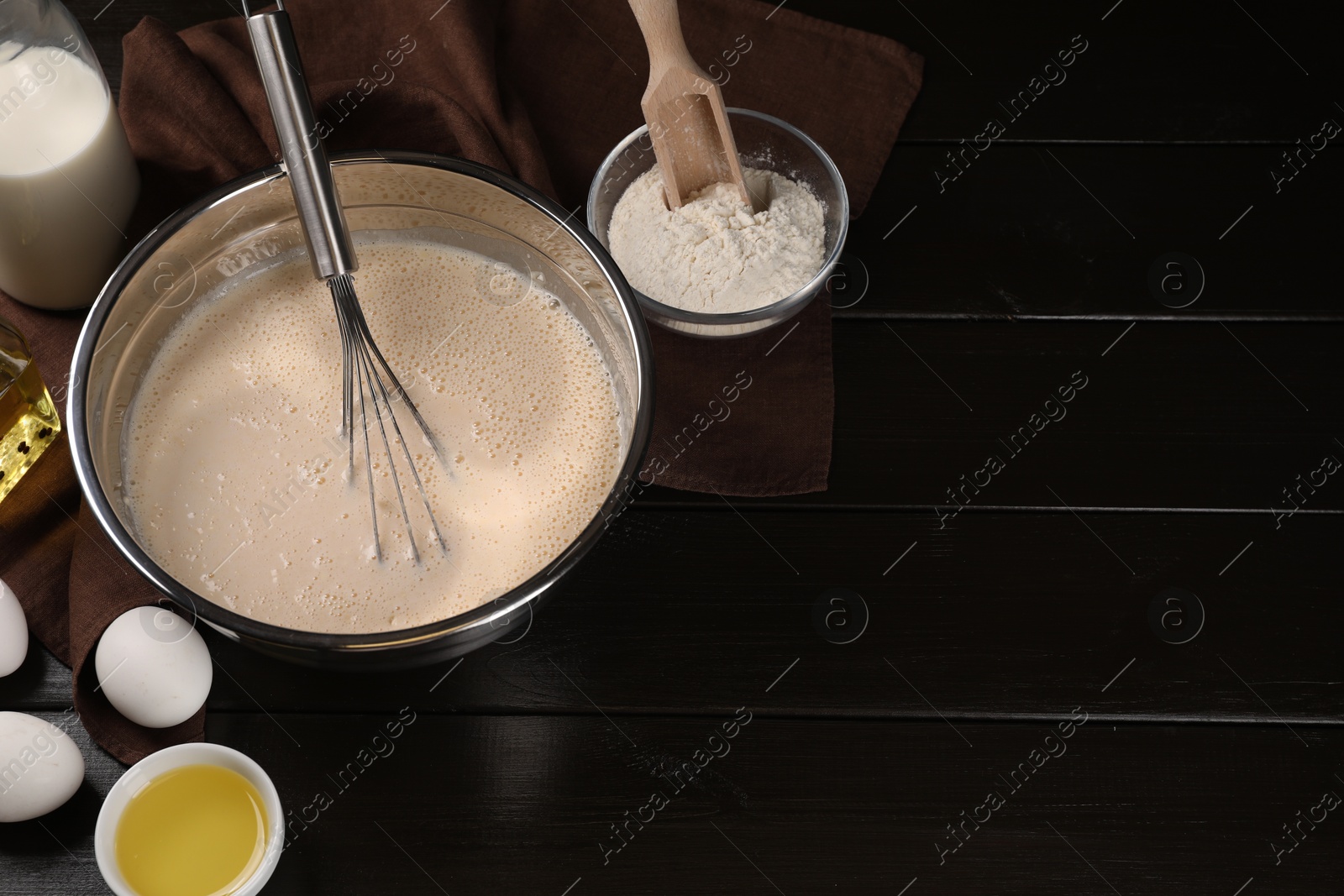 Photo of Dough, metal whisk in bowl and ingredients on dark wooden table, flat lay. Space for text