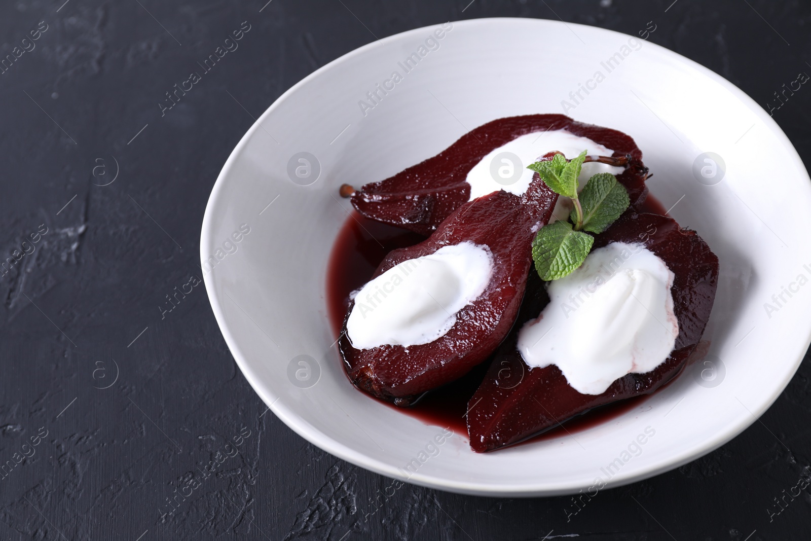 Photo of Tasty red wine poached pears and ice cream on black table, closeup. Space for text