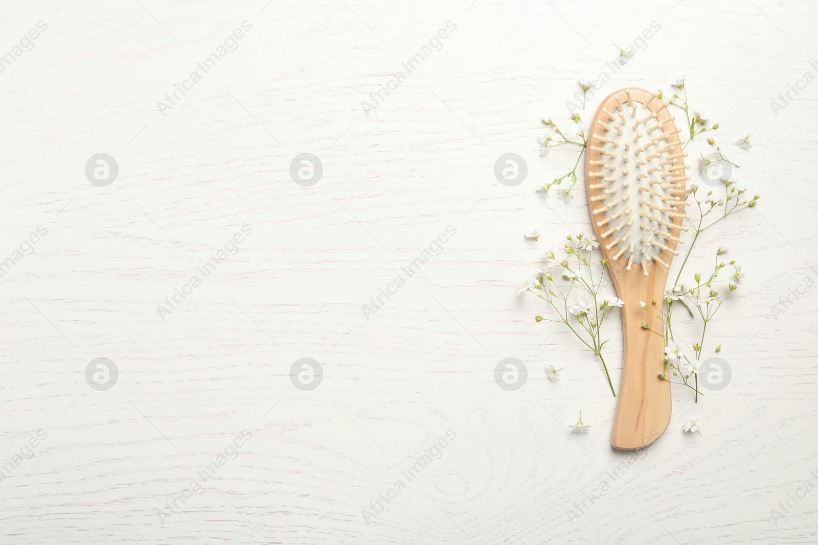 Photo of Hair brush and small flowers on white wooden background, flat lay. Space for text