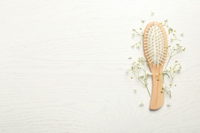 Hair brush and small flowers on white wooden background, flat lay. Space for text