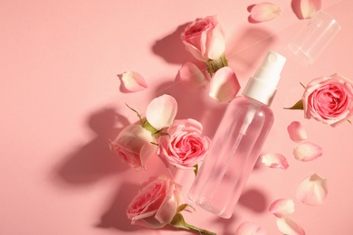 Flat lay composition with rose essential oil and flowers on pink background